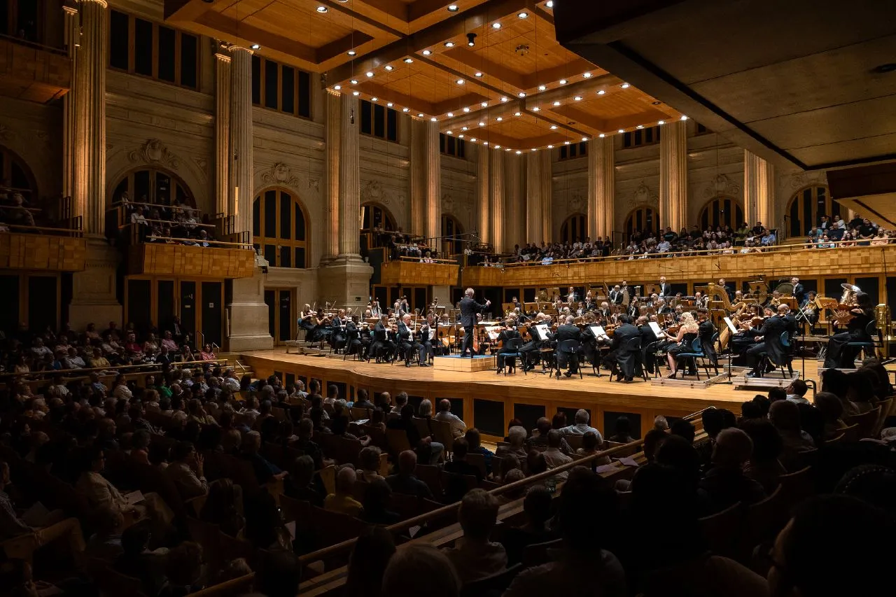 The orchestra on stage at Sala São Paulo, seen from the audience: tall columns, a coffered wooden ceiling, and a full hall.
