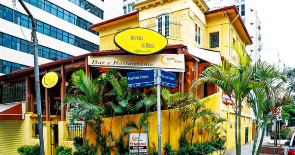 Segredos de Minas on the corner of Rua Bela Cintra: an old yellow house with a terracotta roof, its round yellow sign above the entrance, palms along the wall.